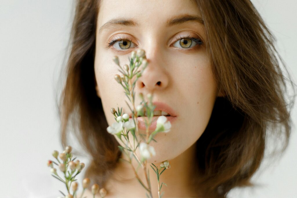 Jeune femme tenant une tige de verdure près de son visage, regardant calmement en face d'elle – symbole de présence, d’ancrage et d’ouverture intérieure, équilibrés avec le balayage oculaire