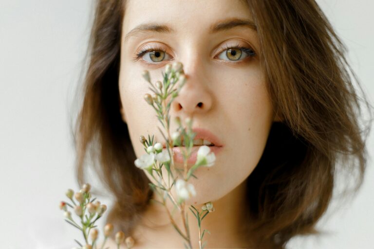 Jeune femme tenant une tige de verdure près de son visage, regardant calmement en face d'elle – symbole de présence, d’ancrage et d’ouverture intérieure, équilibrés avec le balayage oculaire